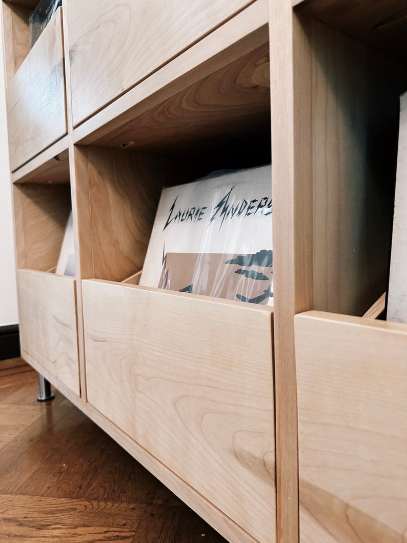 A close up photo of a custom natural birch cabinet's closed drawer with records inside a client's home. There is a Laurie Anderson LP peeking out.