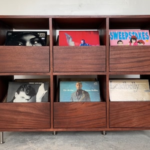 A six-drawer record storage cabinet in a medium brown stain with vinyl records inside the drawers. The legs are chrome.