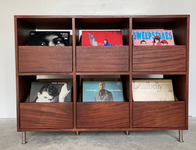 A six-drawer record storage cabinet in a medium brown stain with vinyl records inside the drawers. The legs are chrome.