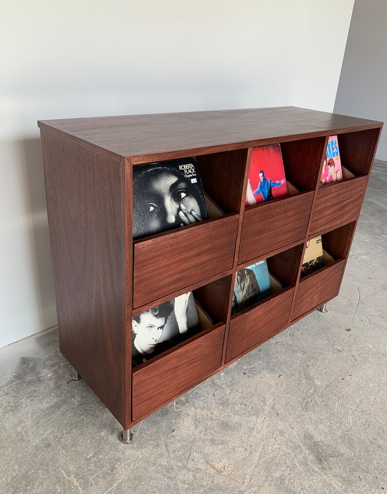 A side view of a six-drawer record storage cabinet in a medium brown stain with vinyl records inside the drawers. The legs are chrome.