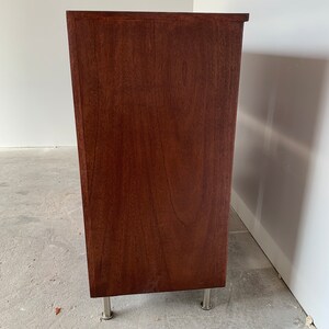 A photo of the side panel of th six-drawer record storage cabinet in a medium brown stain with vinyl records inside the drawers. The legs are chrome.