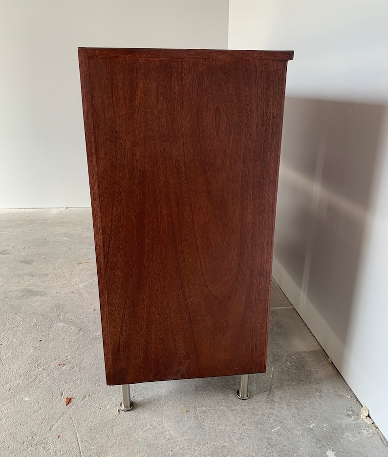 A photo of the side panel of th six-drawer record storage cabinet in a medium brown stain with vinyl records inside the drawers. The legs are chrome.