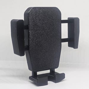 以下が含まれることがあります： 黒色のテクスチャード加工プラスチック製カーフォンホルダー。調整可能なアームと取り付け用のベースを備えています。デザインはシンプルで機能的で、携帯電話をしっかりと保持することに重点を置いています。