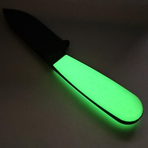 Puede incluir: Un cuchillo negro con un mango verde que brilla en la oscuridad.