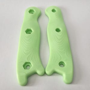 May include: Two light green knife handles with a textured surface and three holes each.