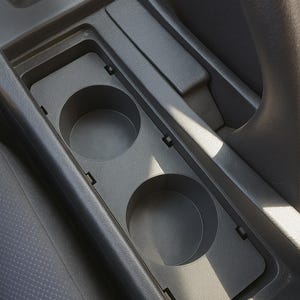 May include: A dark grey car console featuring two circular cup holders. The console is integrated into the vehicle's interior, with a gear stick and steering wheel partially visible. The cup holders are designed to accommodate drinks.