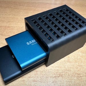 May include: A black external hard drive cooling stand with a blue external hard drive labeled "SAMSUNG Portable" inside.