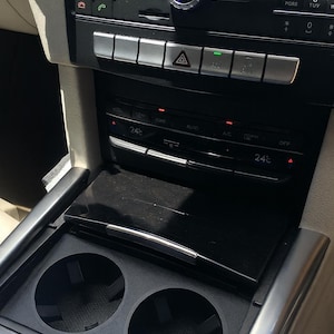 Puede incluir: Panel de control de coche con controles de radio y climatización. Incluye botones para radio, medios y luces de emergencia. El control climático muestra una temperatura de 24 grados Celsius. Con portavasos.