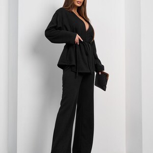 May include: A black two-piece outfit featuring a wrap top with a tie waist and wide-leg pants. The top has a deep V-neckline. The outfit is paired with black pointed-toe heels and a small patterned clutch.