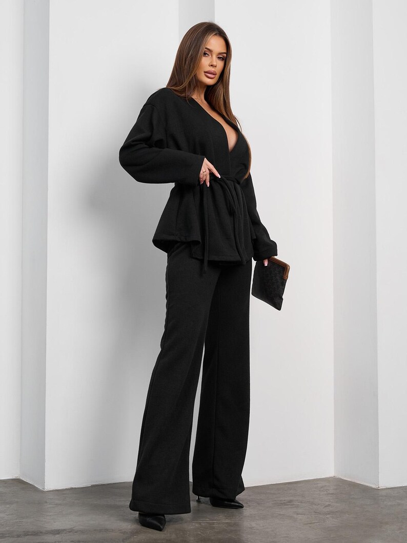 May include: A black two-piece outfit featuring a wrap top with a tie waist and wide-leg pants. The top has a deep V-neckline. The outfit is paired with black pointed-toe heels and a small patterned clutch.