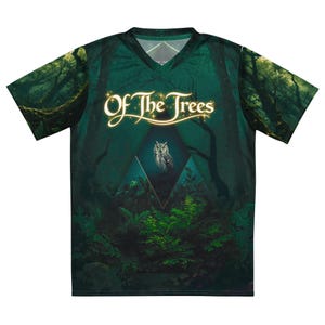 Pode incluir: Uma t-shirt de manga curta com decote em V apresentando um gráfico de floresta verde-escura com uma coruja centrada dentro de um diamante geométrico. O texto "Of The Trees" está impresso numa fonte dourada brilhante no peito.