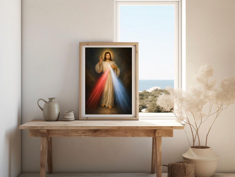 K&ouml;nnte beinhalten: Gerahmtes religi&ouml;ses Kunstwerk, das eine Figur in wei&szlig;en Gew&auml;ndern mit goldenem Heiligenschein zeigt, die rotes und blaues Licht ausstrahlt. Das Kunstwerk wird auf einem Holztisch neben einem Fenster mit Blick auf das Meer ausgestellt.