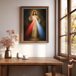 K&ouml;nnte beinhalten: Ein gerahmtes religi&ouml;ses Kunstwerk zeigt eine Figur in wei&szlig;en Gew&auml;ndern mit Heiligenschein, die rotes und blaues Licht ausstrahlt. Das Kunstwerk befindet sich in einem braunen Rahmen und wird an einer wei&szlig;en Wand ausgestellt. Die Szene umfasst einen Holztisch, eine Vase mit Blumen und ein Fenster.