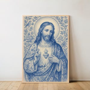 Könnte beinhalten: Ein gerahmter blau-weißer Druck einer religiösen Figur mit Heiligenschein, floralen und Vogelakzenten. Die Figur ist mit langem Haar und Bart dargestellt, trägt ein Gewand und zeigt auf ein Herz. Das Kunstwerk ist vor einem hellen Hintergrund.