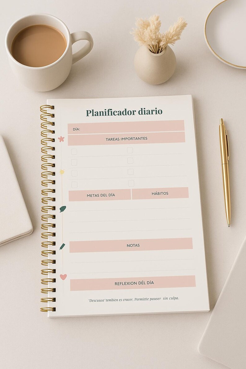May include: A spiral-bound daily planner with gold accents, featuring sections for tasks, goals, and notes. The planner includes text in Spanish, a gold pen, a cup of coffee, and a small vase with dried flowers.