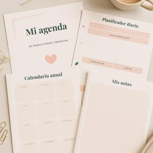 May include: A collection of stationery items, including a daily planner, annual calendar, and notebook. The planner features pink accents and Spanish text. A cup of coffee and decorative sprigs are also present.