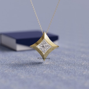 May include: A gold pendant necklace featuring a square-cut diamond set within a four-pointed star design. The pendant hangs from a delicate gold chain. The jewelry is displayed on a blue surface with a blurred background.