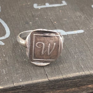 Puede incluir: Un anillo de plata con un diseño cuadrado que presenta las iniciales "QW" grabadas en la parte superior.