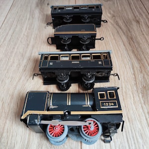 Op de afbeelding: Een verzameling vintage speelgoedtreinwagons. De set bevat een zwarte locomotief met rode wielen en het nummer 1234, samen met verschillende passagierswagons. De treinwagons zijn zwart met gouden accenten.