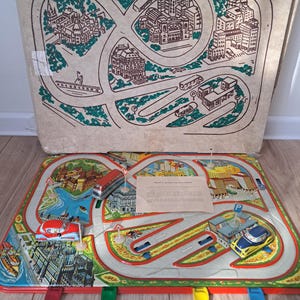 May include: Vintage toy city play set with a cardboard map featuring roads, buildings, and a river. The set includes toy cars, buses, and street signs. The play set is on a wooden surface.