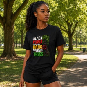 May include: A black short-sleeved t-shirt featuring the text "BLACK PEOPLE DON'T HANG THEMSELVES FROM TREES" in white, red, yellow, and green lettering, accompanied by a graphic of a green tree with a red prohibition circle symbol overlaid.