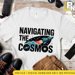 Puede incluir: Camiseta blanca con un diseño gráfico negro de una nave espacial volando por el espacio con el texto "Navigating the Cosmos".