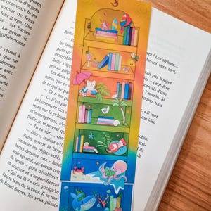 Peut inclure: Marque-page coloré avec une illustration de bibliothèque. Le design comprend des livres, un perroquet, une pieuvre et des créatures marines. Un accessoire charmant pour les lecteurs.