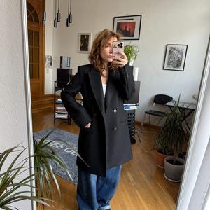May include: A black double-breasted blazer with a classic design. The blazer has a tailored fit and features two rows of buttons. The model is wearing the blazer with blue jeans. The blazer is a versatile piece for any wardrobe.