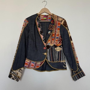 May include: A dark grey blazer with colourful patchwork detailing. The blazer has a single button closure and gold trim. The sleeves and lapels feature intricate patterns, creating a unique and artistic design.