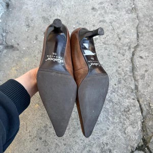 May include: A pair of brown leather high heels with pointed toes and stiletto heels. The soles are dark brown, and the heels are black. The brand name "Gabor Fashion" is printed on the insole. The shoes are size 5 1/2.