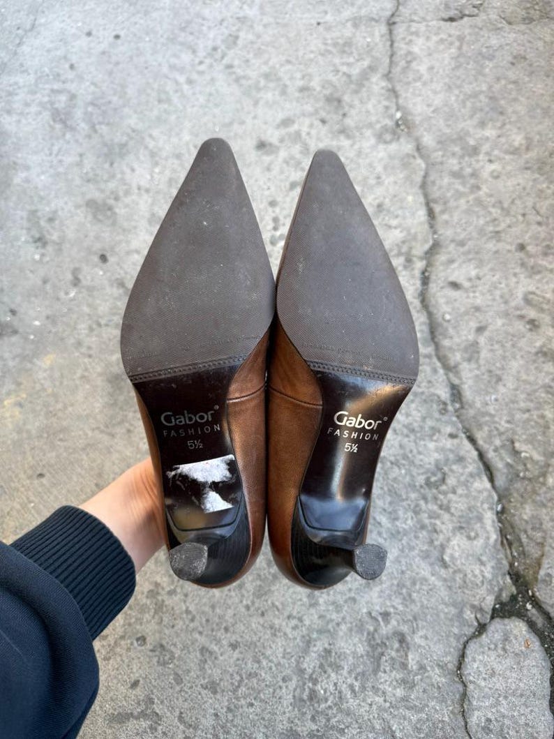 May include: A pair of brown leather Gabor Fashion heels, size 5 1/2, with pointed toes and small heels. The soles are dark brown, and the heels are black. The shoes are held up, showing the soles and heels.