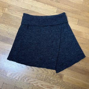 May include: A dark gray knitted skirt with a wrap-around design and a wide waistband.
