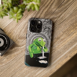 May include: A smartphone case featuring a green frog character positioned against a black and white circular mandala pattern. The frog is depicted with a white straw and white powder lines on a black surface at the bottom of the case design.