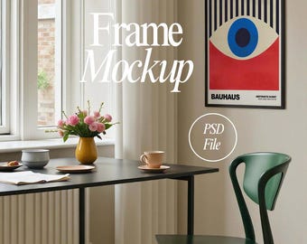 May include: A black framed poster with a red, white, and blue abstract eye design. The poster is hanging on a beige wall above a black table with a green chair. The text on the poster reads "BAHAUS" and "ABSTRAKTE KUNST".