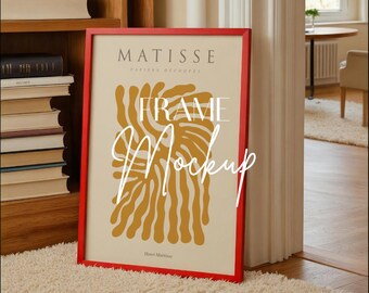 May include: A red framed art print featuring a Matisse design with the text "FRAME Mockup". The artwork has a cream background with orange abstract shapes. The frame is leaning against a wall on a cream colored rug.
