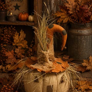 May include: A fabric pumpkin figure with a cream-colored body, a tall orange hat featuring dark polka dots, and a burlap accent. The figure has triangular fabric eyes and a rectangular mouth, topped with dried straw and a small metal bell.