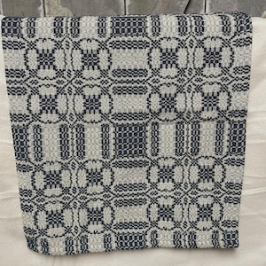 May include: A woven textile featuring a repeating geometric pattern in dark charcoal and off-white. The design consists of interconnected squares and rectangular blocks, creating a structured, grid-like appearance across the entire fabric surface.