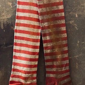 May include: A pair of red and white striped stockings with a faded and worn look. The stockings are hanging on a wooden surface.