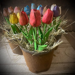 May include: A group of colorful faux tulip flowers in brown pots with straw-like filler. The tulips are red, yellow, blue, and brown.