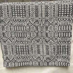 May include: Black and white woven throw blanket with a geometric pattern. The blanket is made of a soft, textured fabric.