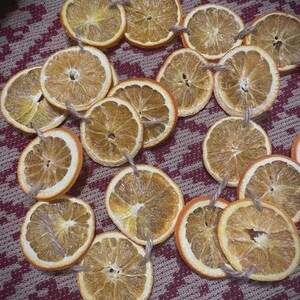 Puede incluir: Rodajas de naranja secas con lazos de cuerda, dispuestas sobre una superficie estampada. Las rodajas de naranja tienen un aspecto natural y r&uacute;stico, con texturas y variaciones de color visibles. Ideales para manualidades o decoraci&oacute;n.