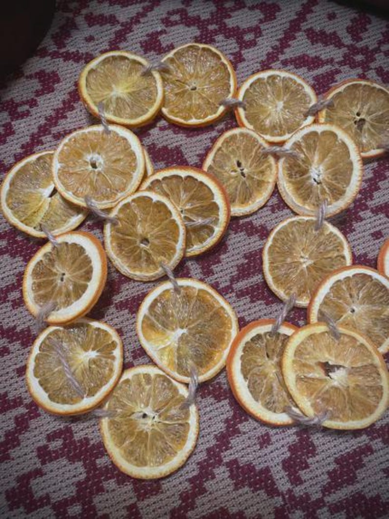 Puede incluir: Rodajas de naranja secas con lazos de cuerda, dispuestas sobre una superficie estampada. Las rodajas de naranja tienen un aspecto natural y r&uacute;stico, con texturas y variaciones de color visibles. Ideales para manualidades o decoraci&oacute;n.
