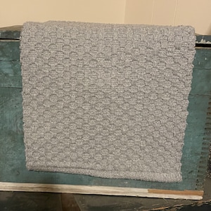May include: A gray woven rug with a textured pattern. The rug is laying on top of a wooden crate.