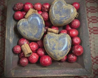 May include: A rustic wooden tray filled with red decorative berries, cinnamon sticks, and three heart-shaped ornaments. The ornaments are blue with a distressed, aged appearance. The tray has a dark, weathered finish.