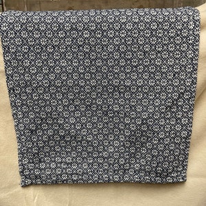 May include: Folded navy blue and white patterned fabric. The fabric features a repeating geometric design of white floral shapes on a navy blue background. The fabric is folded over.