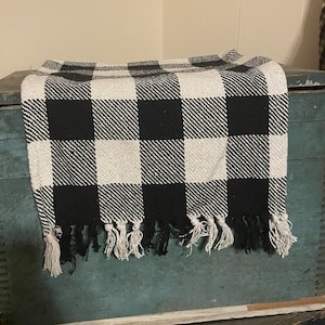 May include: Black and white checkered throw blanket with fringe. The blanket is draped over a wooden box with a blue painted surface.