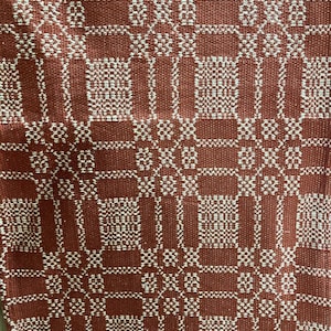 May include: A red and white woven throw blanket with a geometric pattern. The blanket has a square design with a repeating pattern of squares and diamonds.