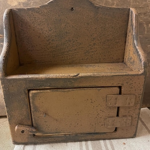 May include: A rustic wooden wall-mounted cabinet with a hinged door and a shelf. The cabinet is painted in a brown and black distressed finish.