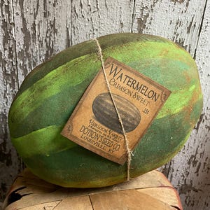 Puede incluir: Una sand&iacute;a decorativa con rayas verdes y verde oscuro, atada con hilo. Una etiqueta dice "Watermelon Crimson Sweet" y "Dotson's Seed Co. Louisville, KY."