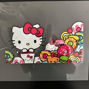K&ouml;nnte beinhalten: Ein wei&szlig;er Hello Kitty Charakter mit einer roten Schleife h&auml;lt eine Tasse Kaffee. Der Hintergrund ist gef&uuml;llt mit bunten Donuts, Cupcakes und anderen s&uuml;&szlig;en Leckereien.